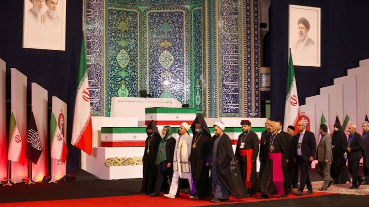 Khamenei funeral crowds filling a Mashhad street with red flags near the golden shrine