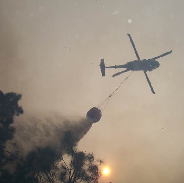 British Columbia wildfire response shown by a helicopter dropping water through wildfire smoke
